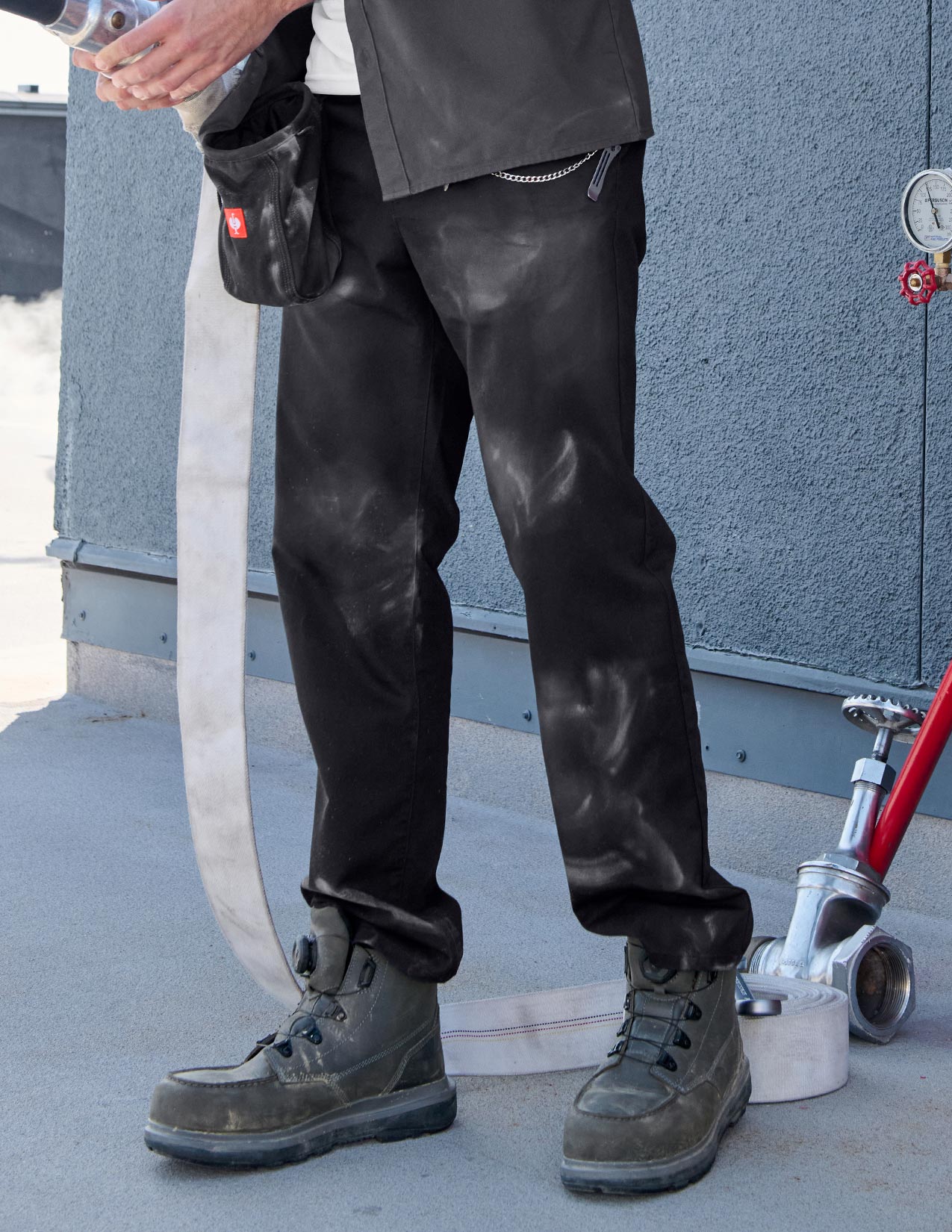 Person wearing black pants and work boots near a building.