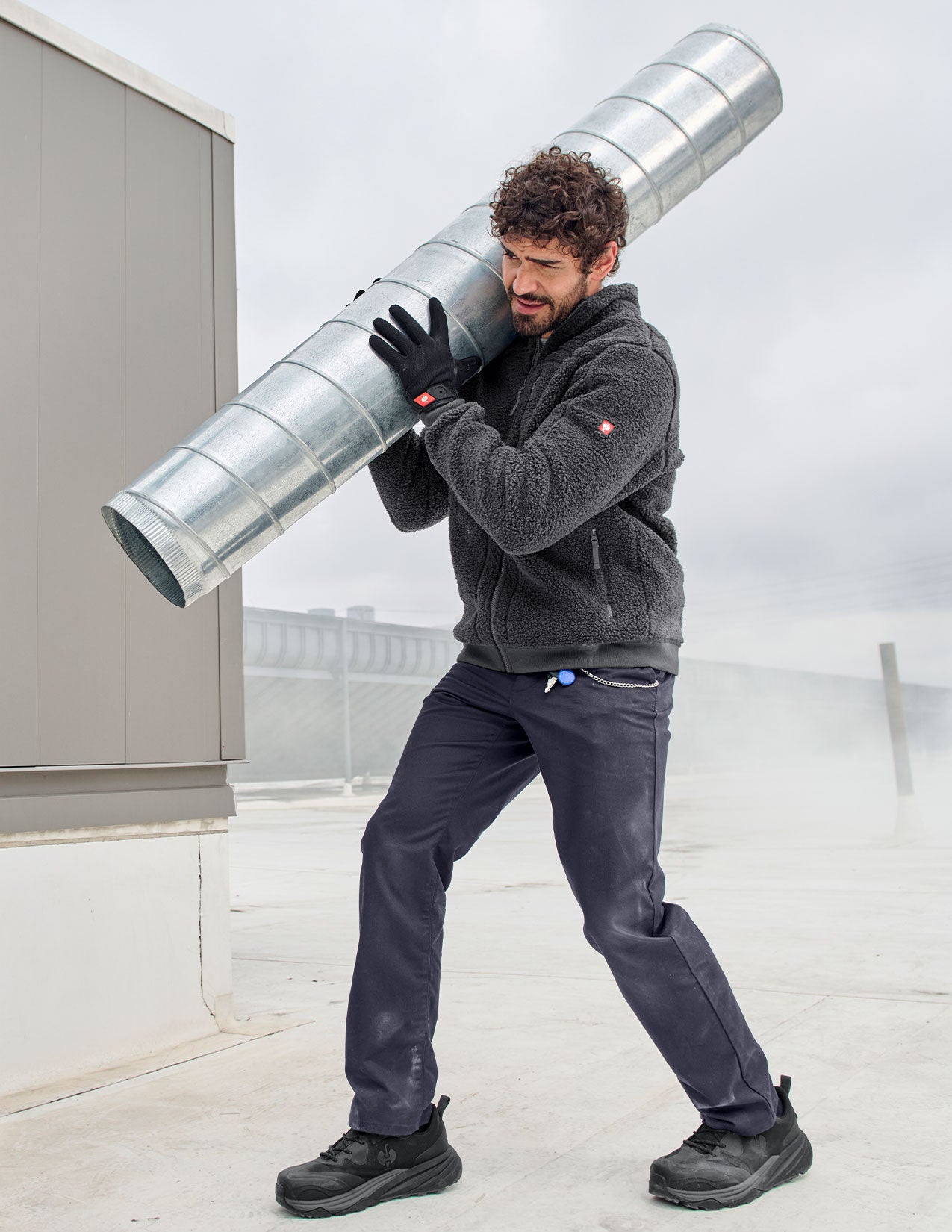 Person carrying a large metal barrel against a light background