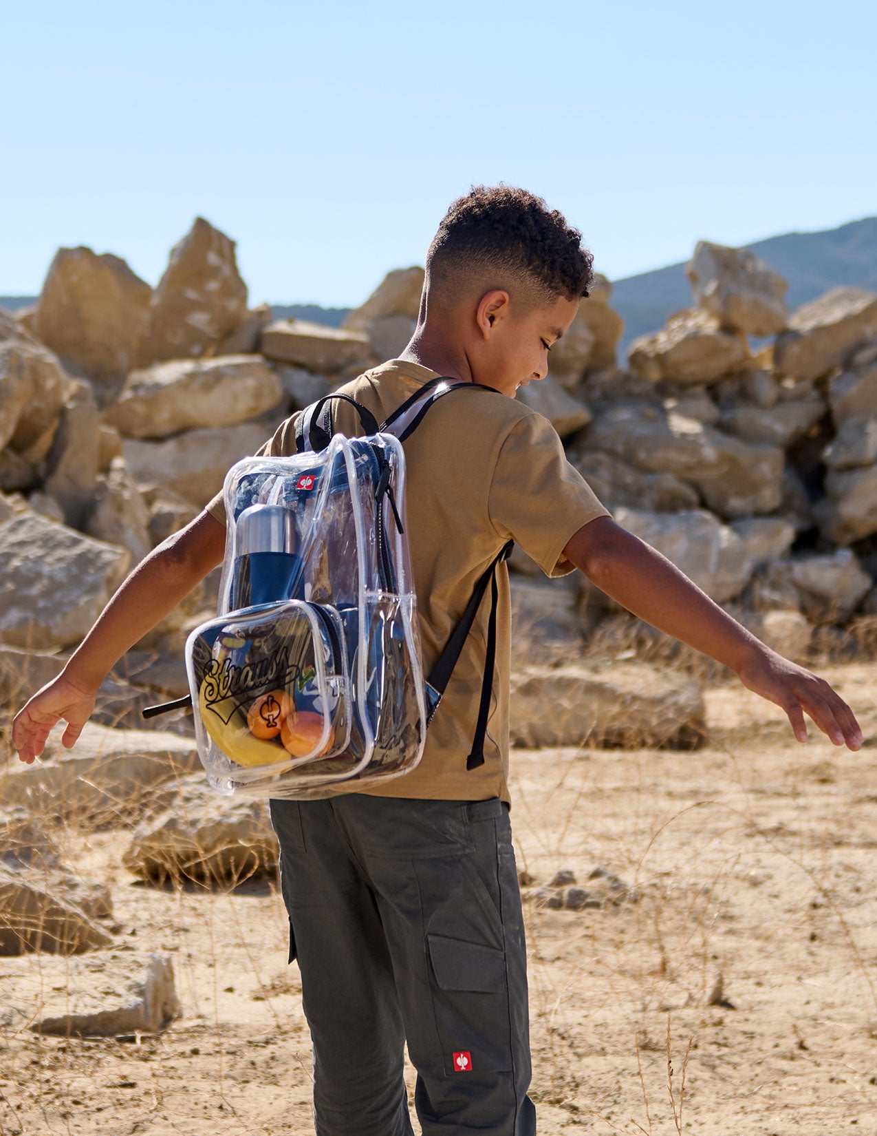 Person wearing a transparent backpack in a desert-like setting with rocky landscape.