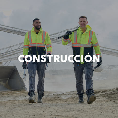 Two construction workers in high-visibility jackets walking on a construction site with the word 'CONSTRUCCIÓN' displayed.
