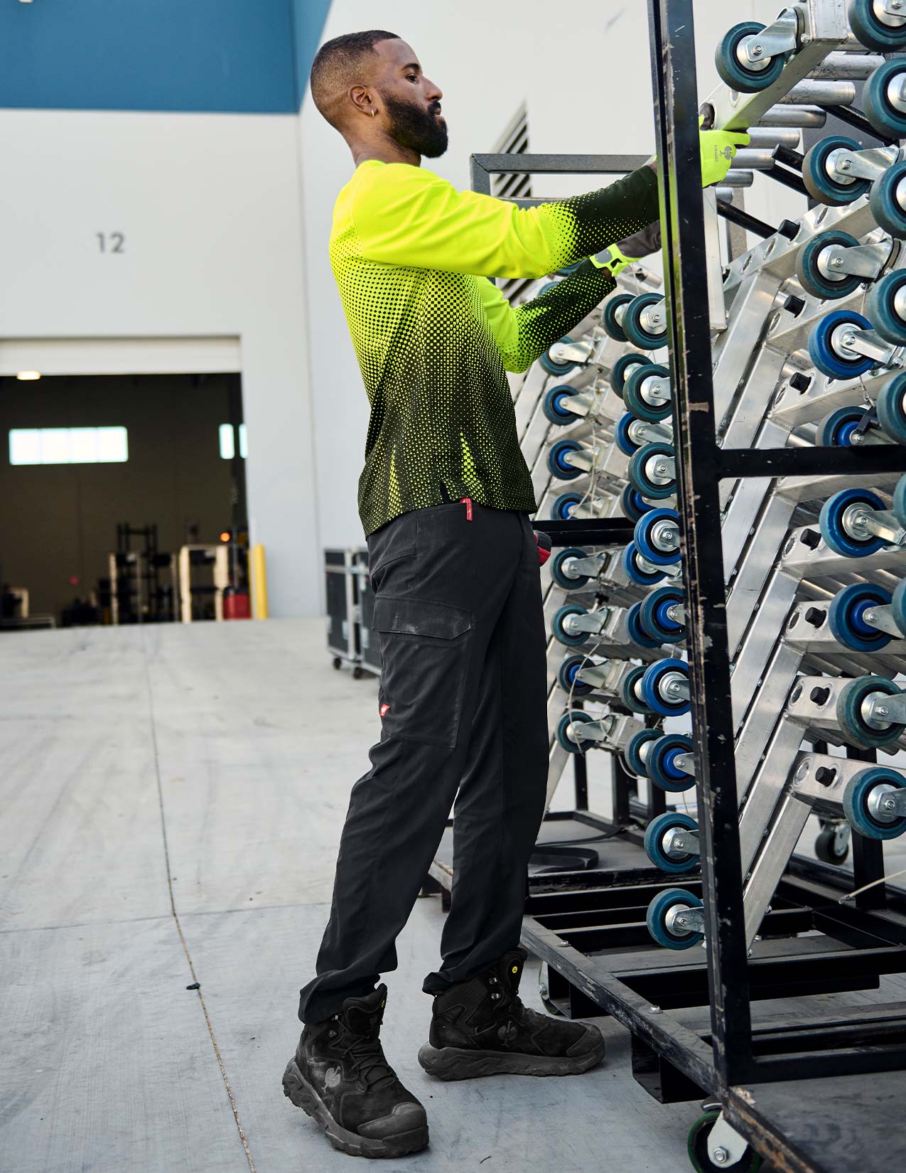 Person in a bright yellow safety shirt and black pants working with equipment in an industrial setting.