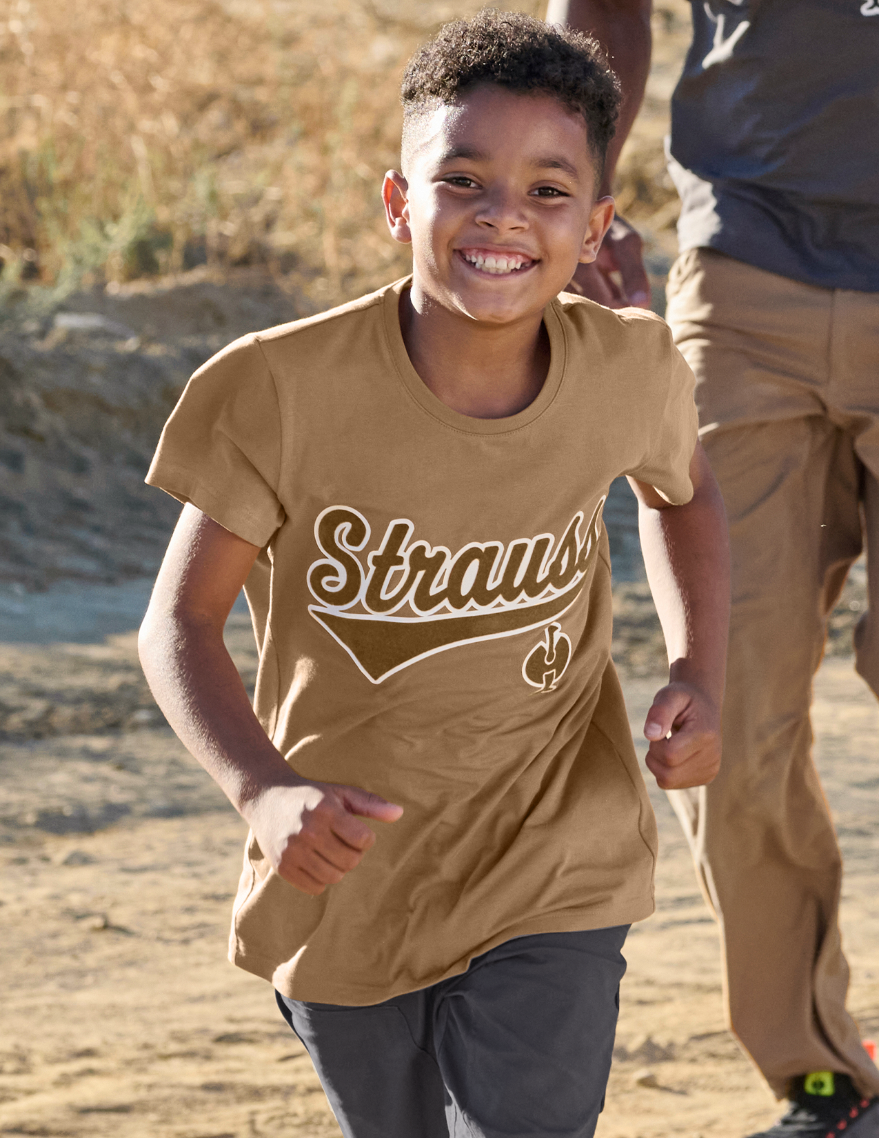 Child wearing a tan 'Strauss' t-shirt outdoors