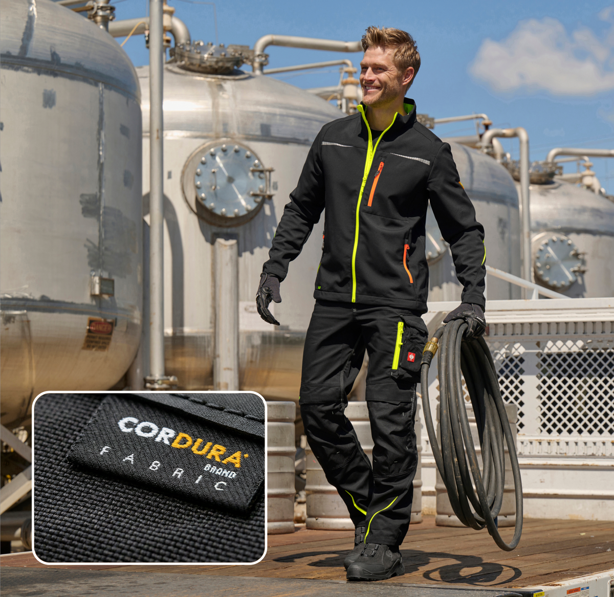 A man in black workwear with neon accents stands near industrial tanks holding a hose. Inset shows a close-up of a Cordura Fabric label on the clothing.