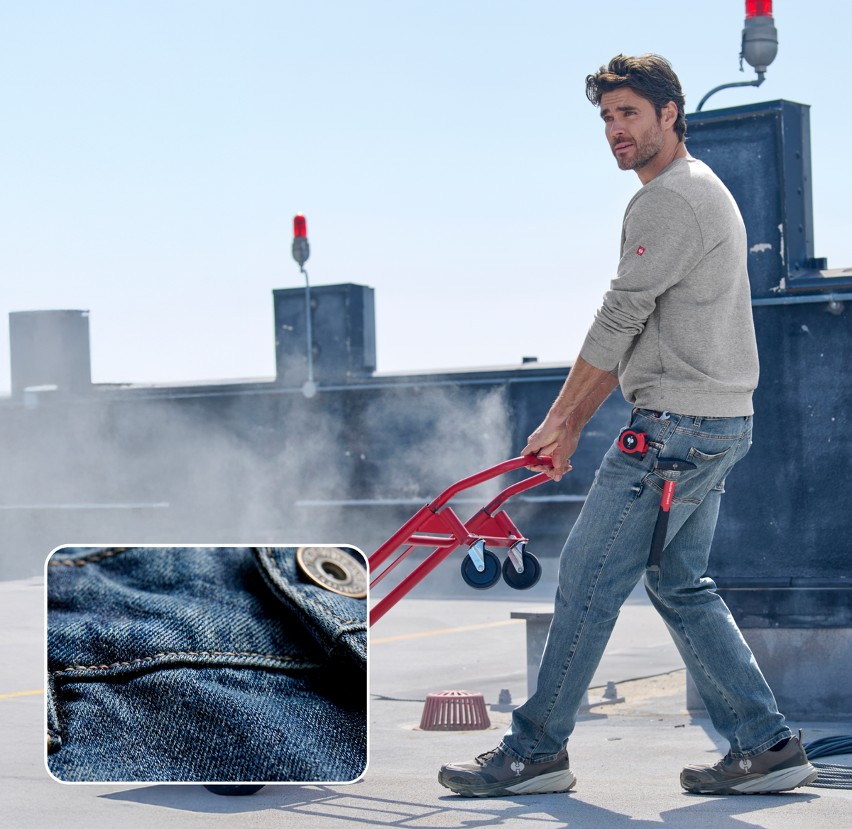 A man in a gray sweater and jeans uses a red hand truck on a rooftop; an inset shows a close-up of denim fabric and a button on the jeans.