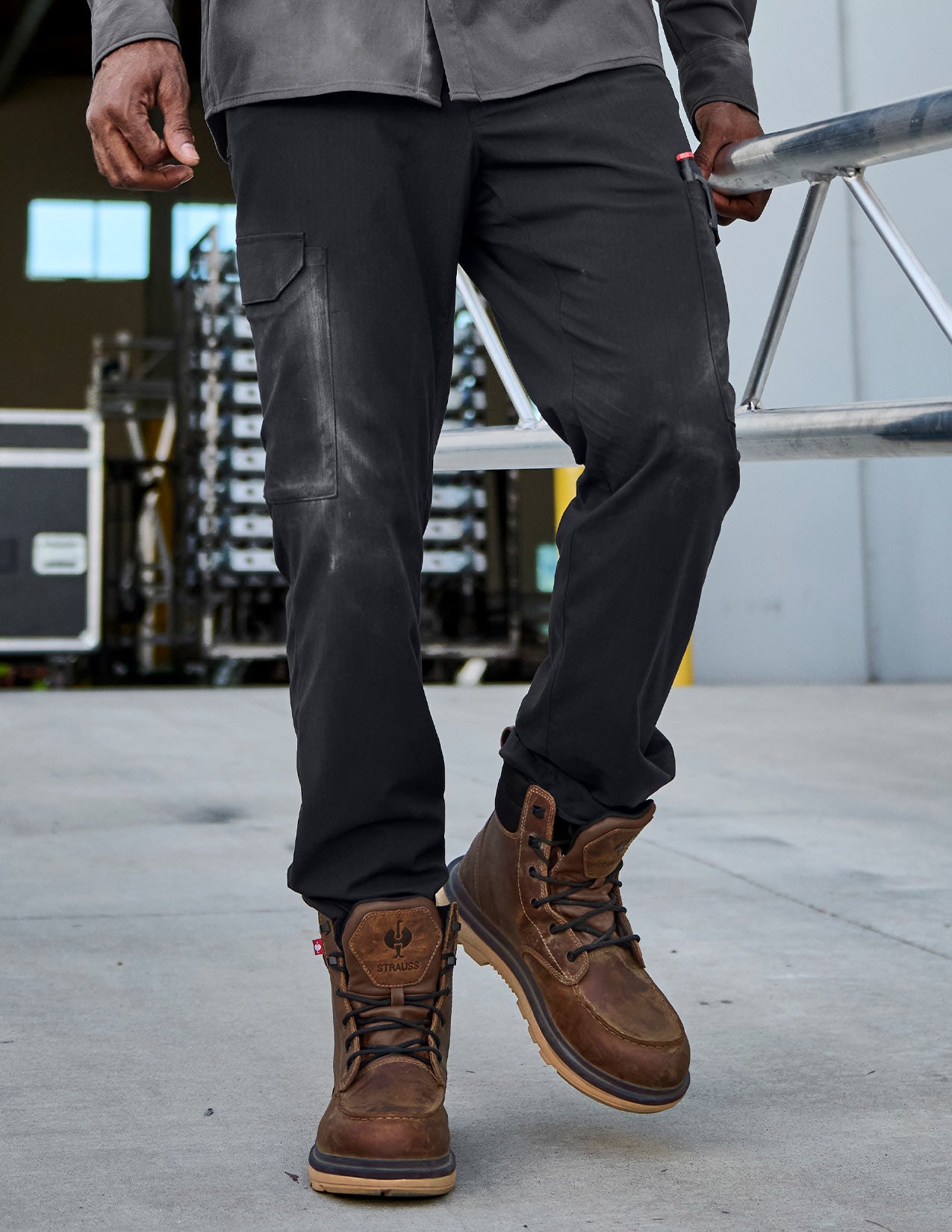 Person wearing black pants and brown boots standing on a concrete surface with industrial background