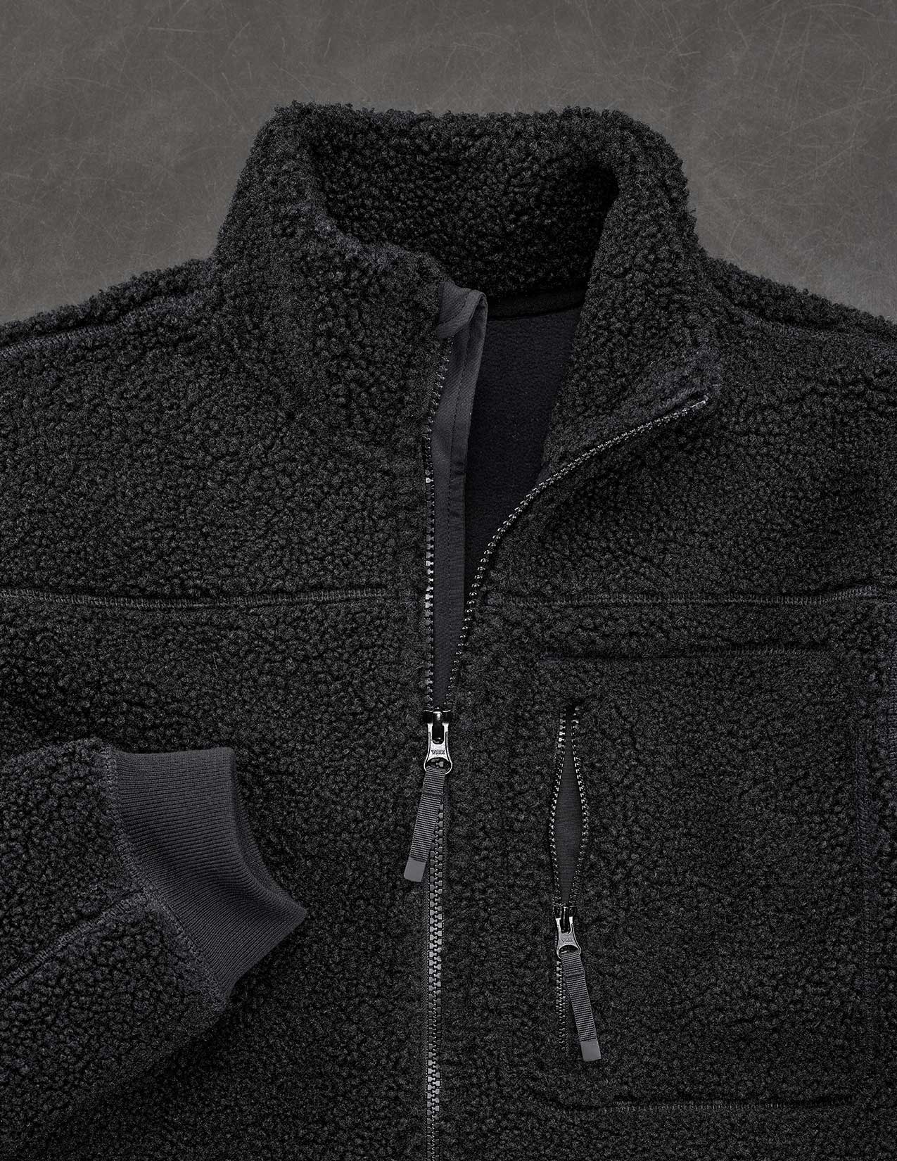 Black fleece jacket with zippers on a dark gray background