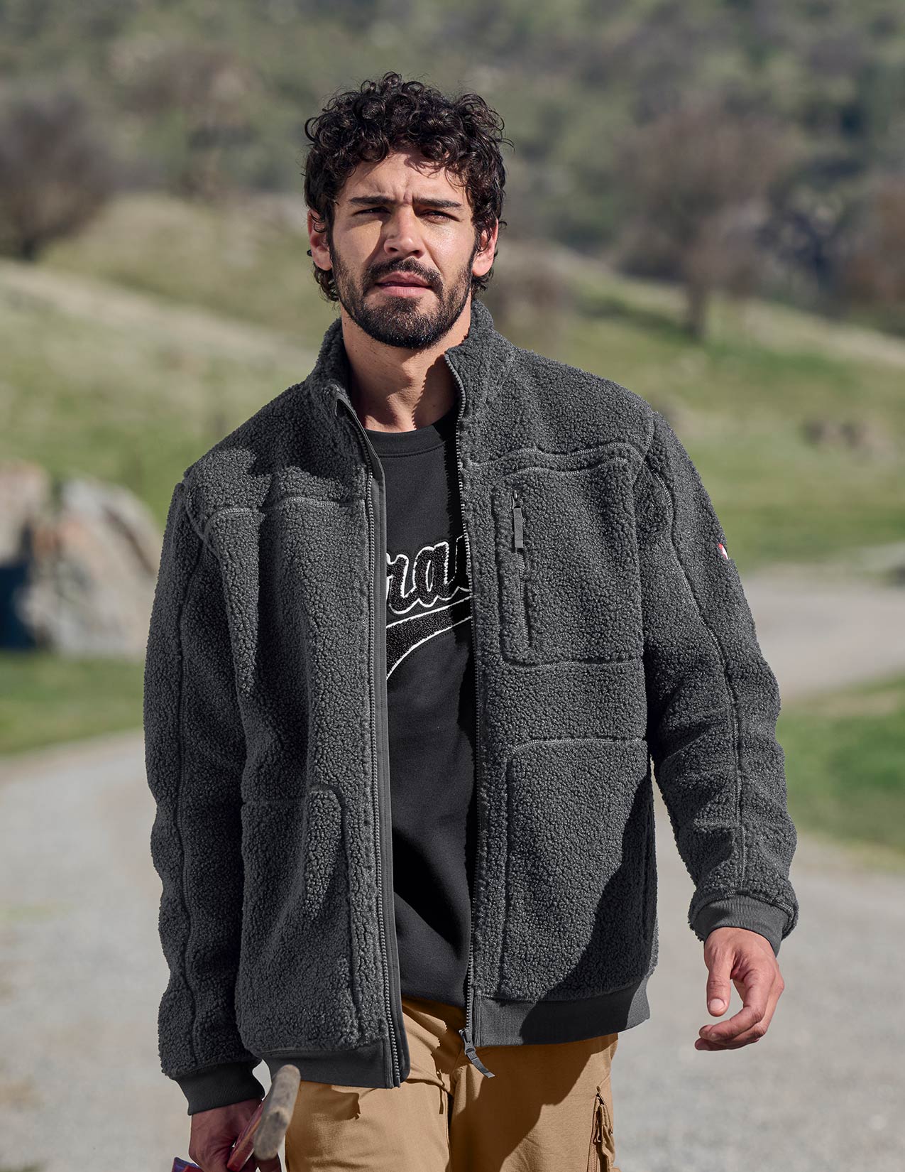Man wearing a dark gray jacket outdoors with greenery in the background