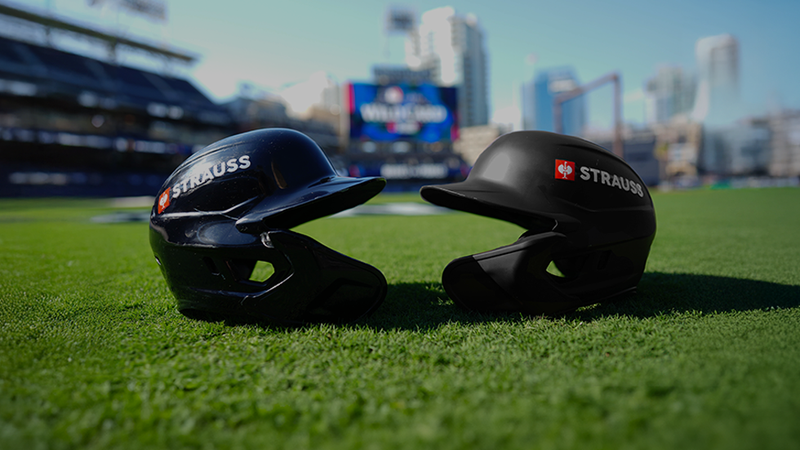 Two baseball helmets face each other with the Strauss logo on them.