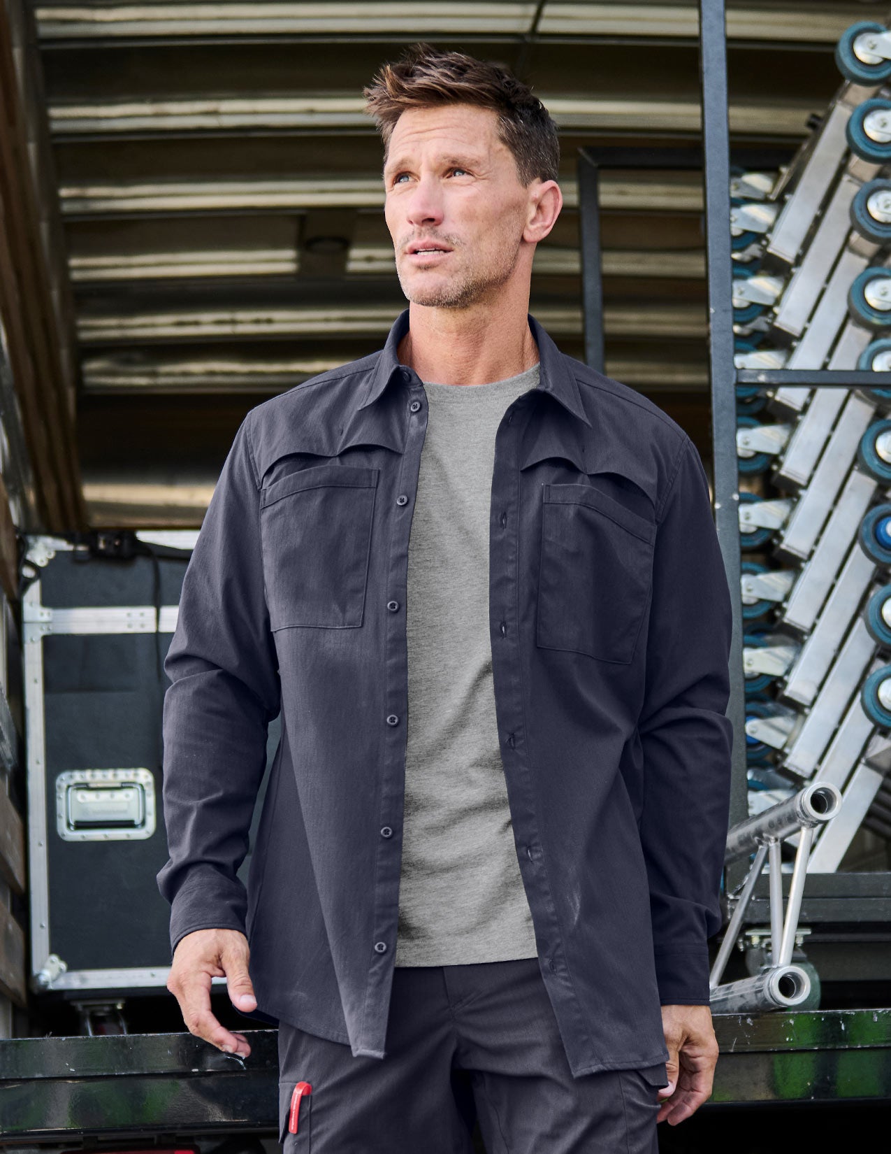 Man wearing a dark blue work shirt and gray shirt standing in front of industrial equipment.