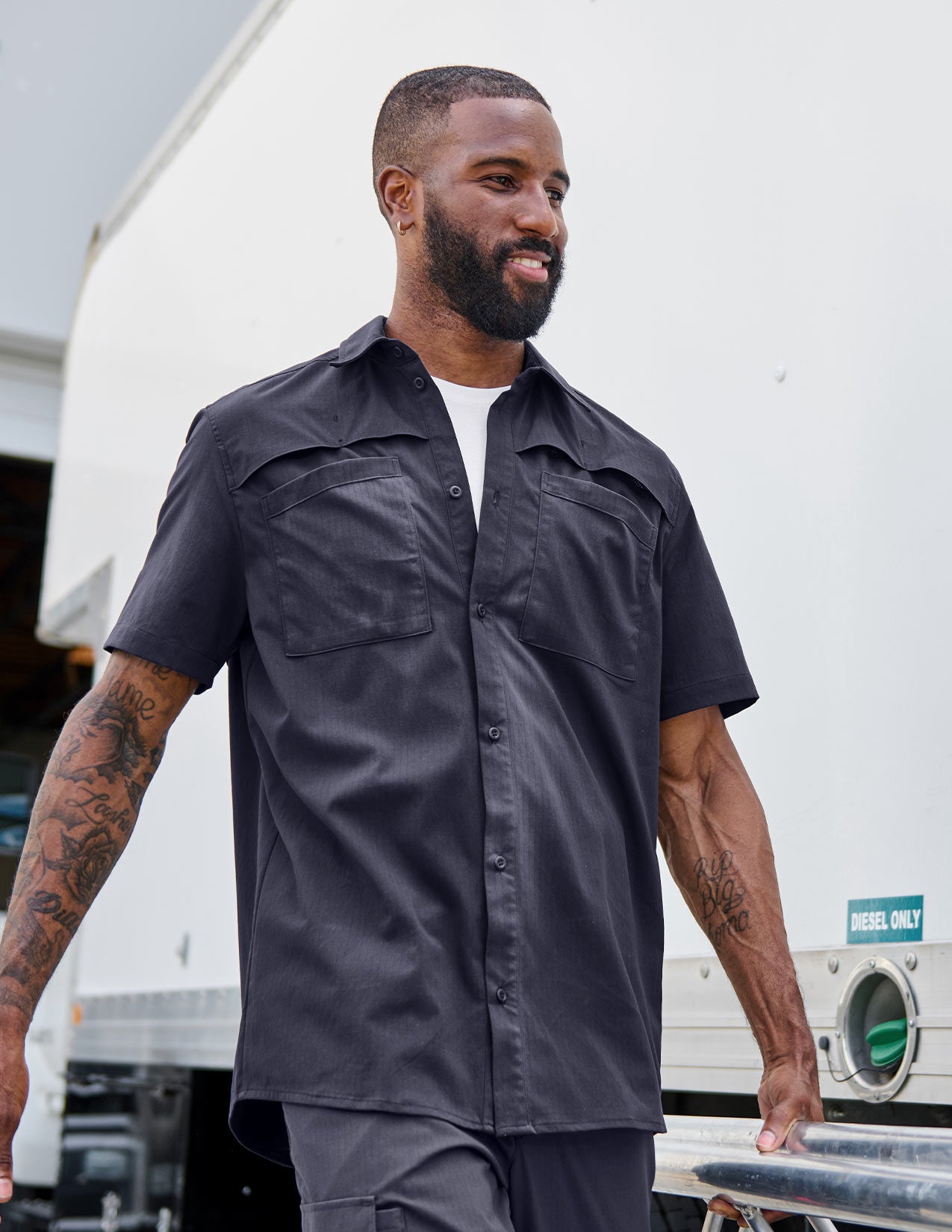 Man wearing a dark blue work shirt, standing in front of a truck
