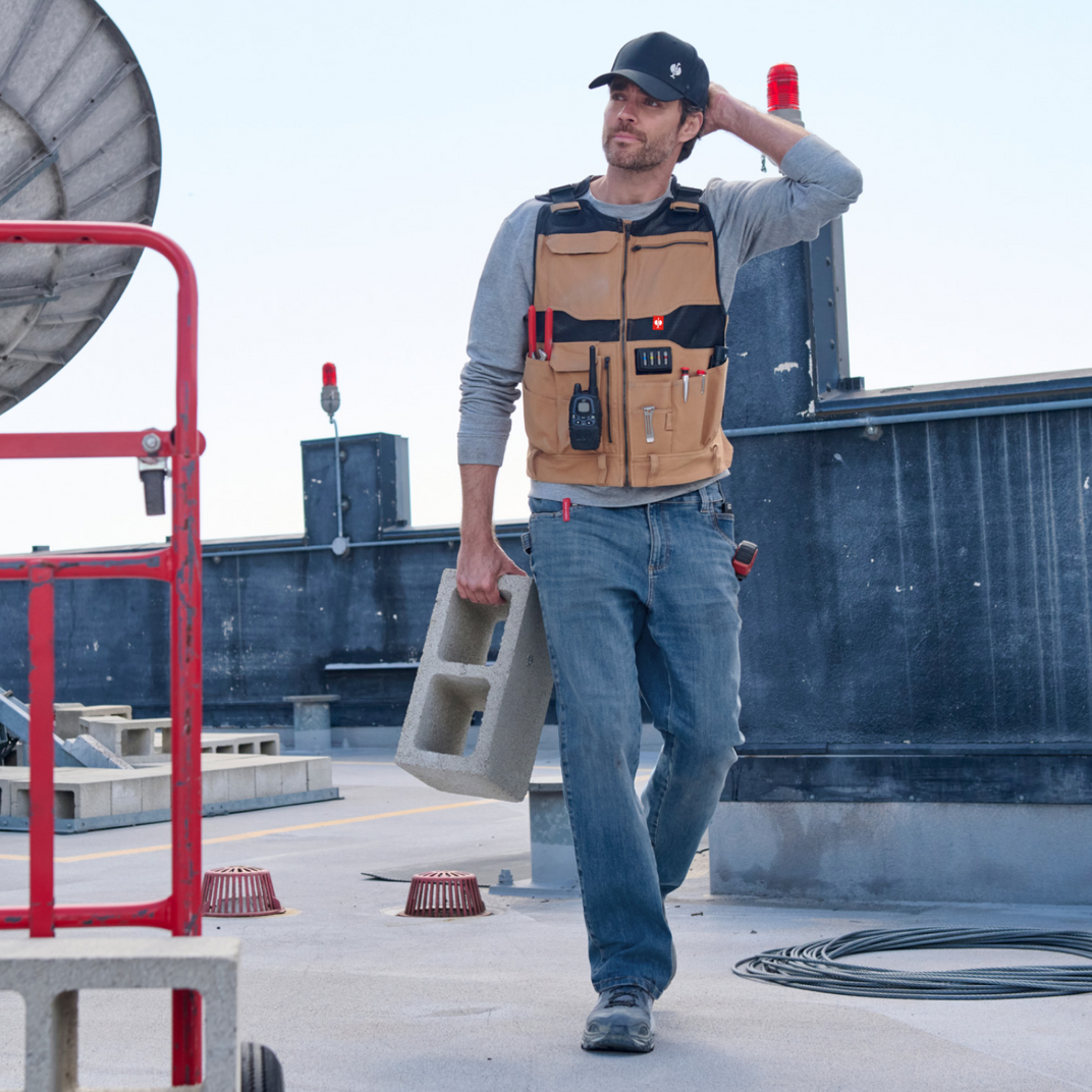 Man on a rooftop wearing a tool vest and carrying a concrete block.