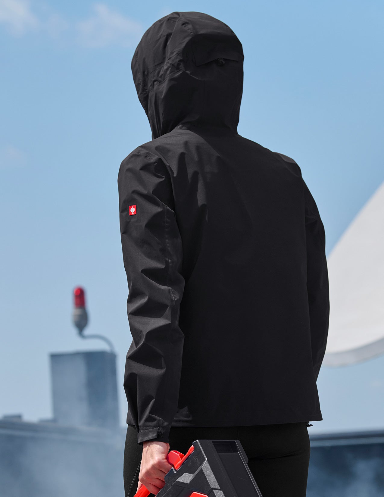 Person wearing a black winbreaker against a blue sky.