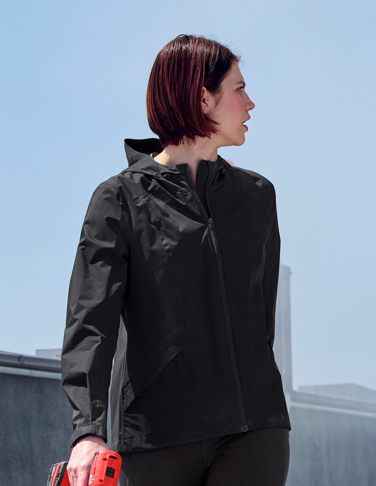 Woman wearing a black jacket on a rooftop with a clear blue sky.
