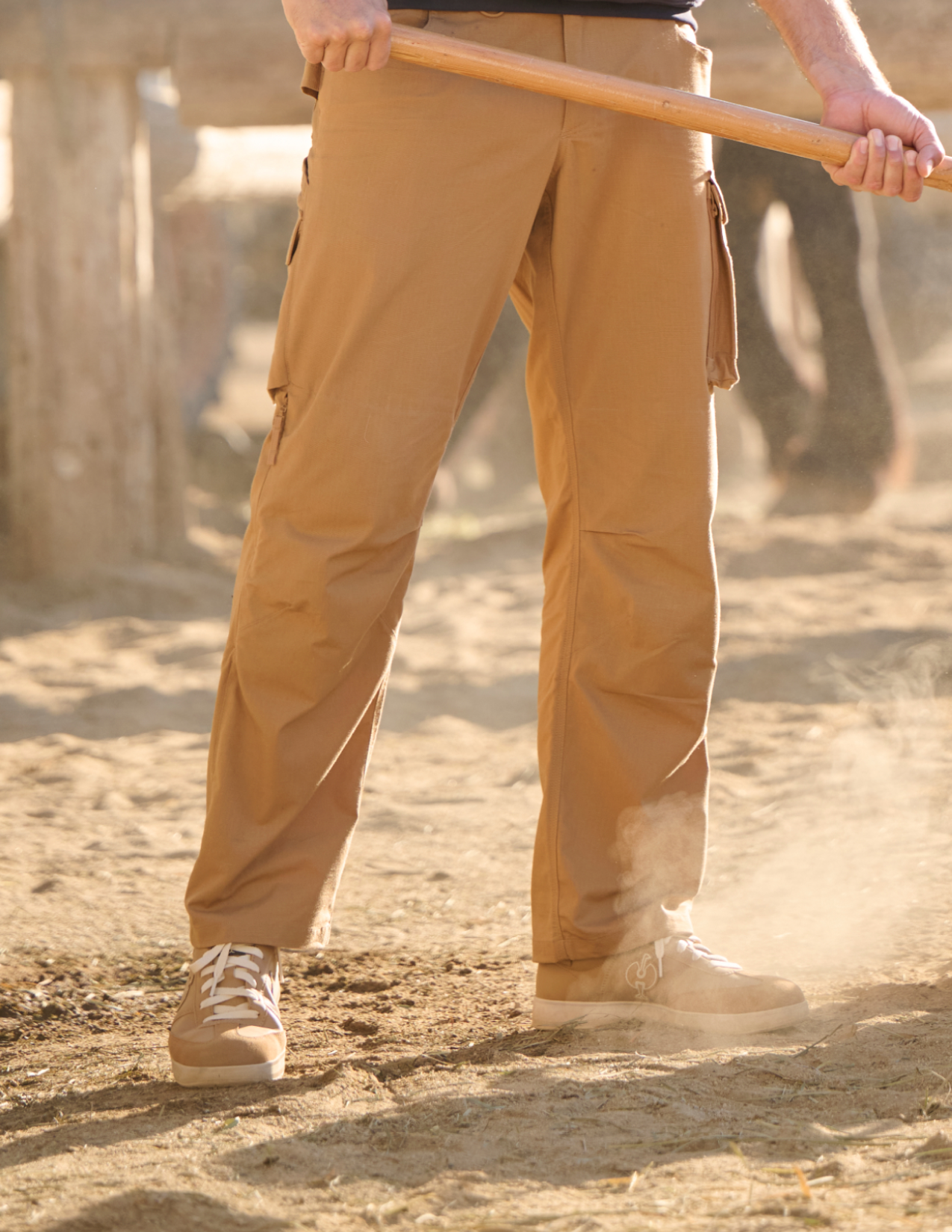 Person wearing beige pants and shoes standing on a sandy surface with a blurred background