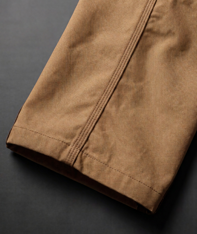 Close-up of a tan canvas garment sleeve or cuff with double-stitched seams, shown on a dark gray background.