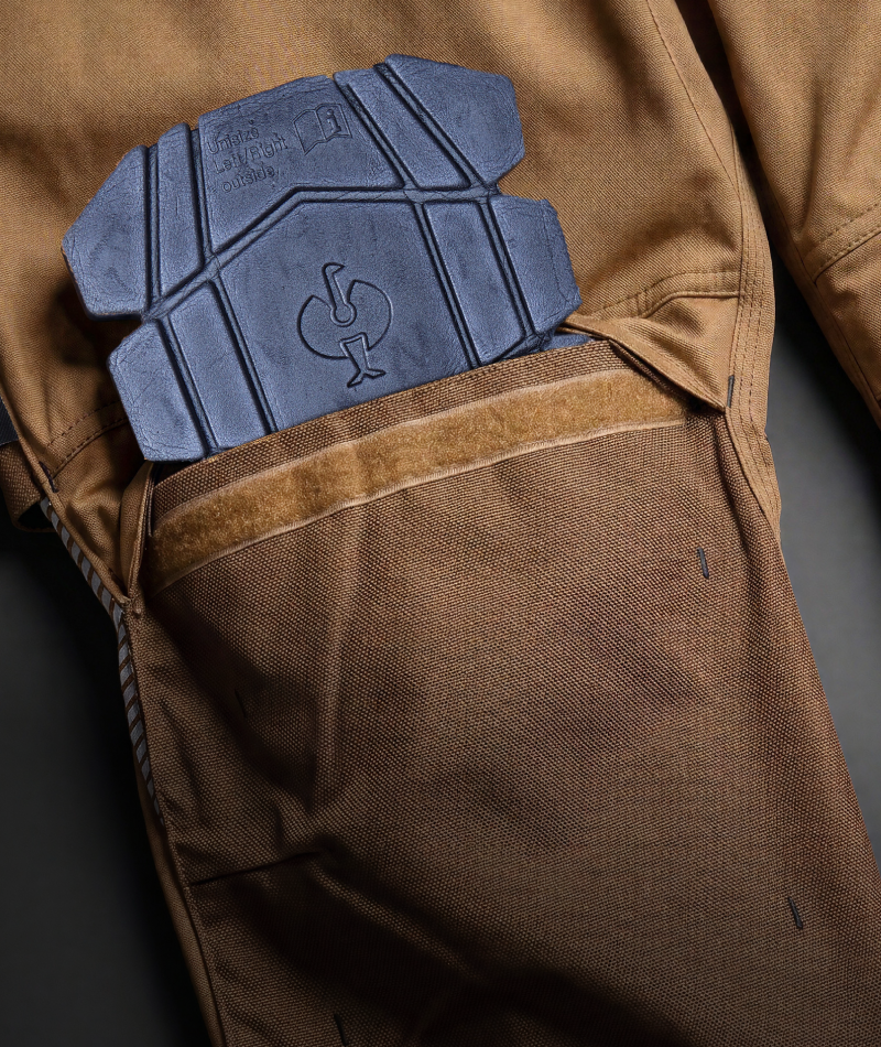 Close-up of a brown technical jacket or pants pocket showing a dark gray protective pad or insert with an embossed logo, set against a dark background.