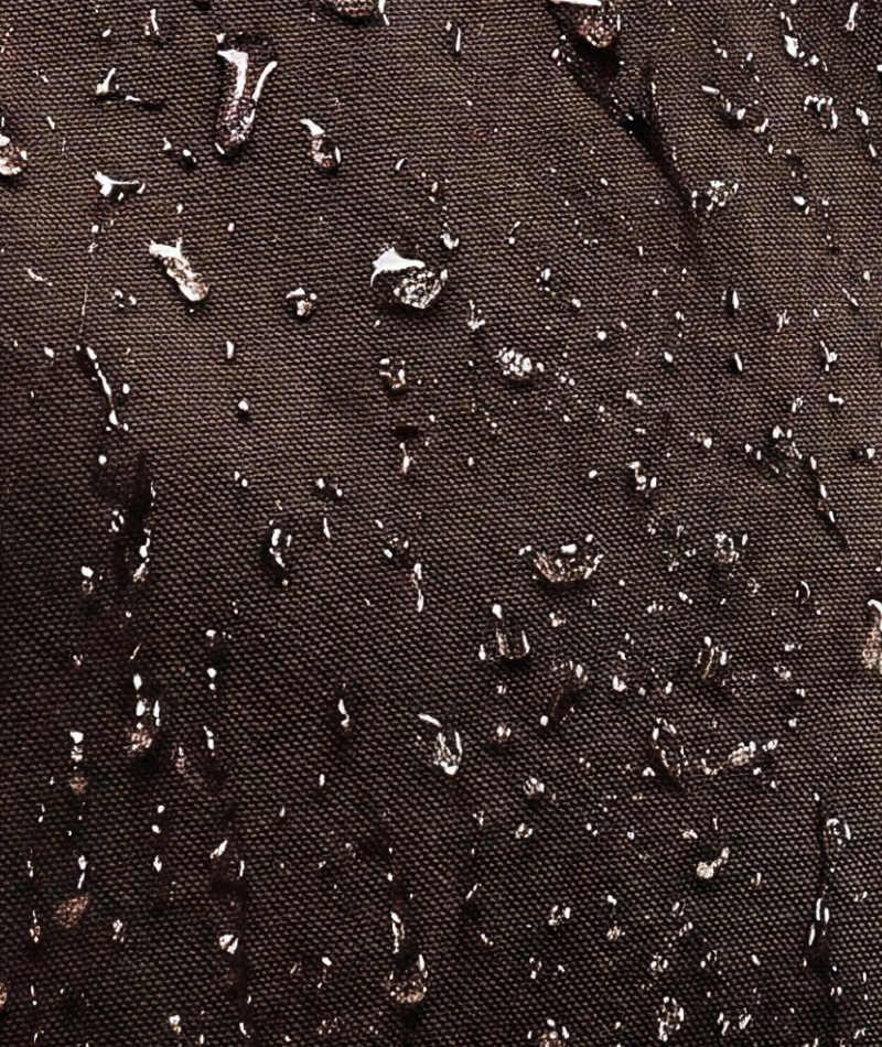 Close-up of a dark brown textured fabric surface with scattered water droplets on a waterproof coating.