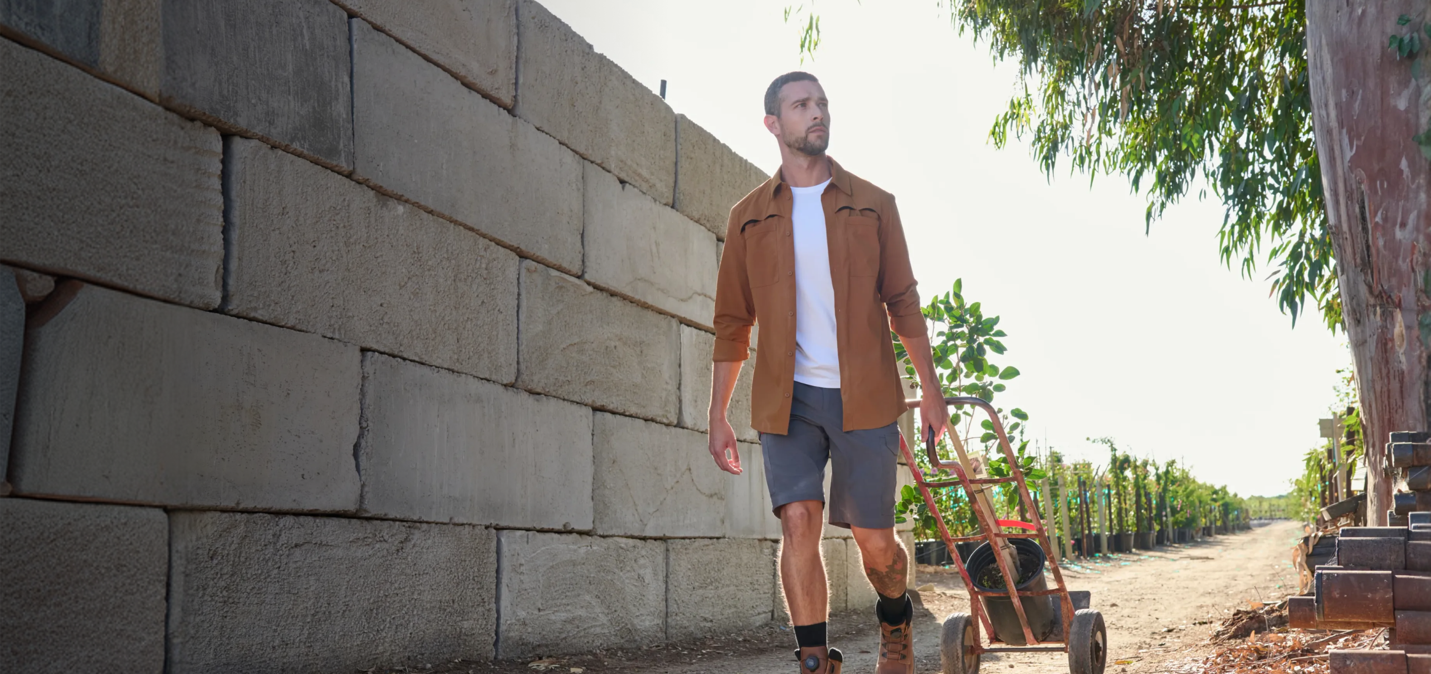 Man walking with a small cart on a path next to a stone wall