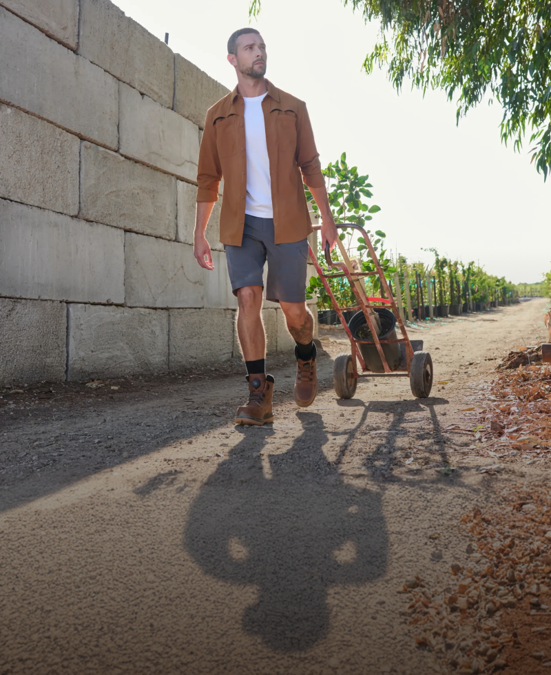 Man walking with a small cart on a path next to a stone wall