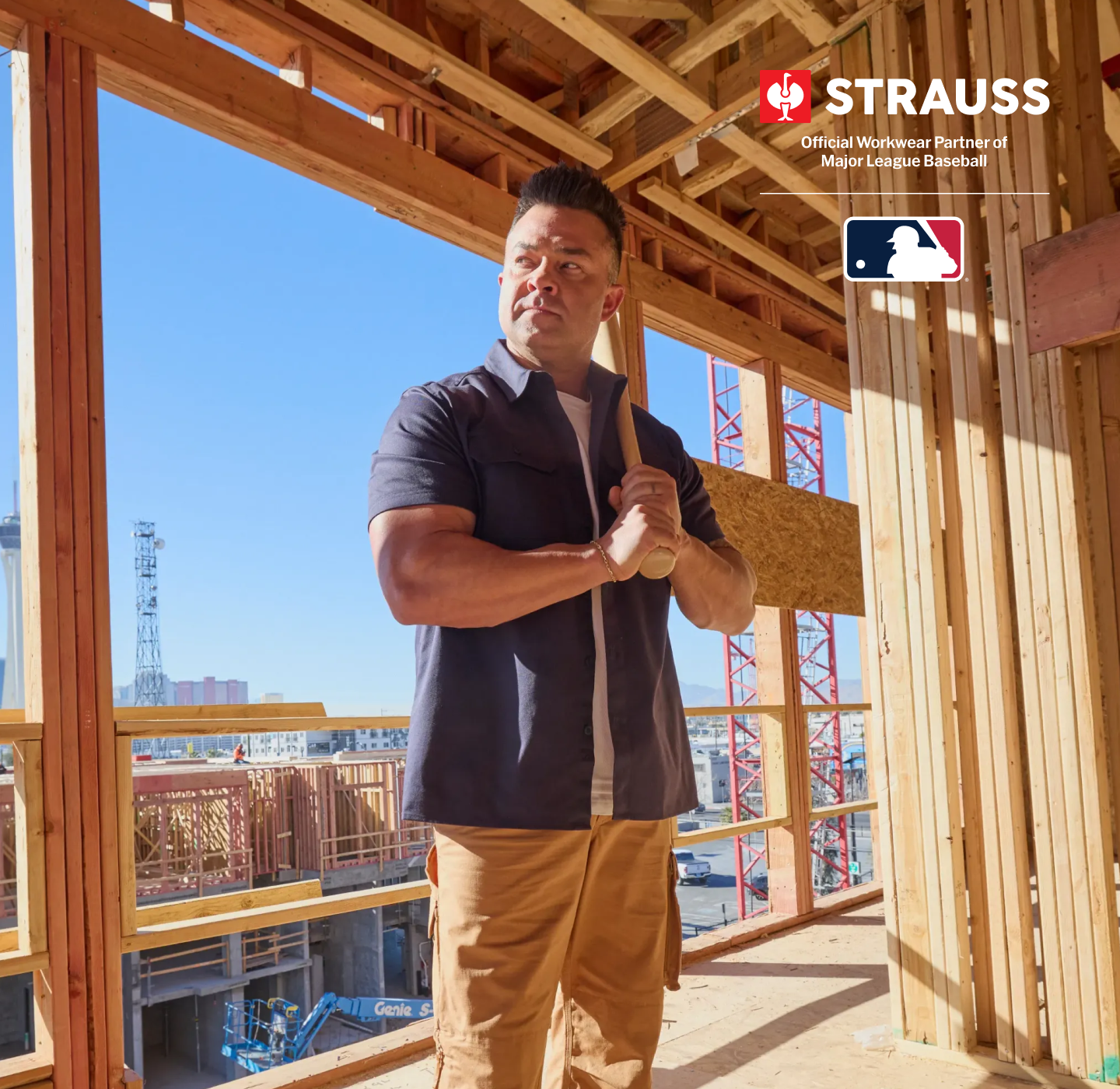 Nick Swisher stands on a construction site inside a wooden framing structure, holding a baseball bat. He is wearing a dark navy short-sleeve button-up shirt and tan cargo pants. On the top right corner the STRAUSS and MLB logo is displayed.