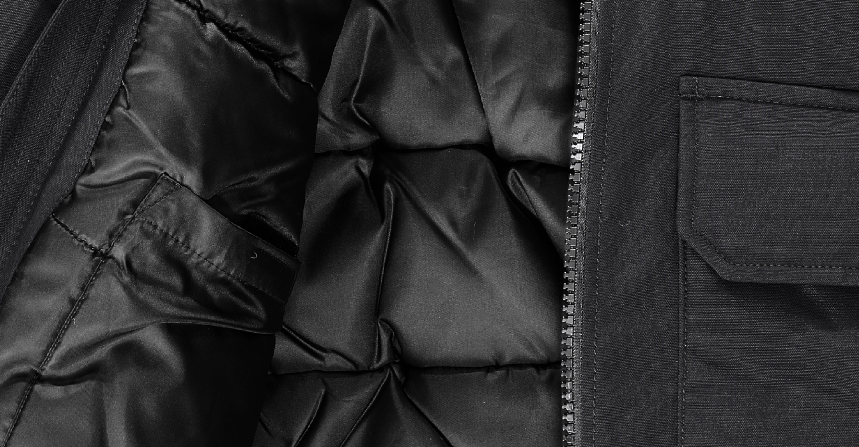 Close-up of a black winter jacket, showing a quilted inner lining, a zipper, part of an outer pocket, and detailed stitching on the fabric.