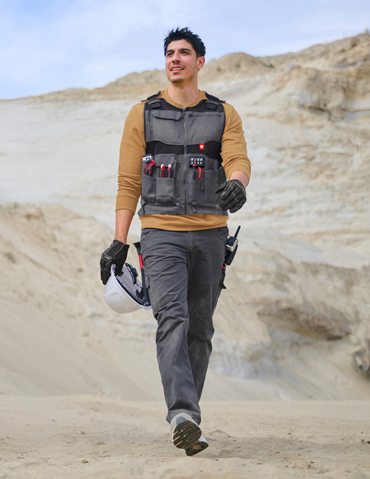 Person wearing a tool vest and holding a helmet in a desert setting